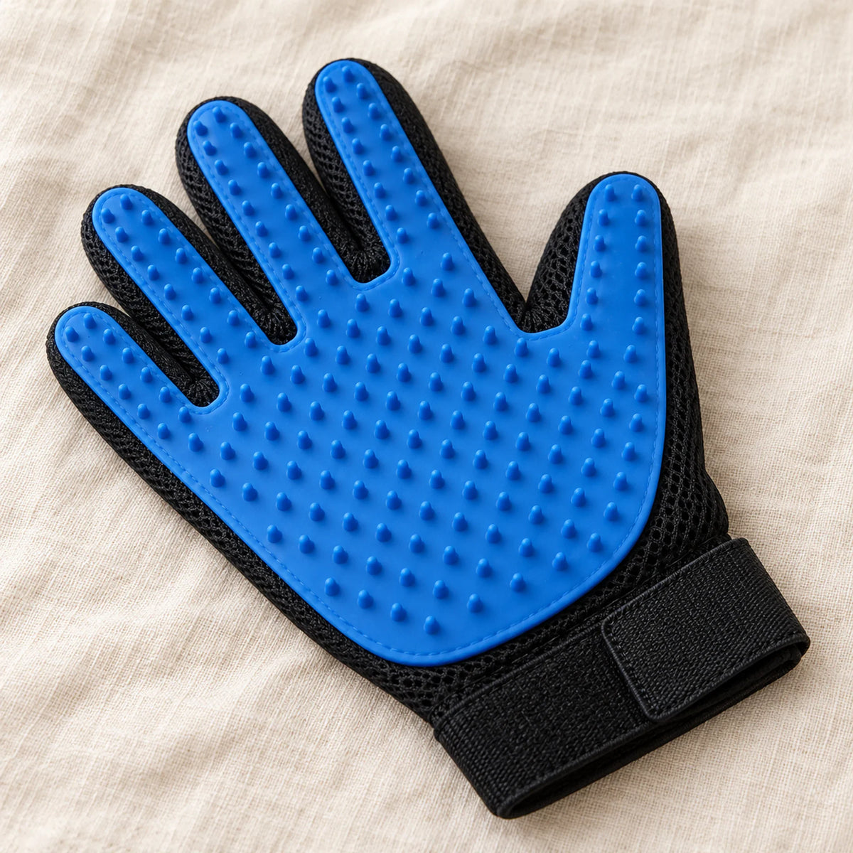 Blue silicone pet grooming glove with a black mesh back on a beige linen surface
